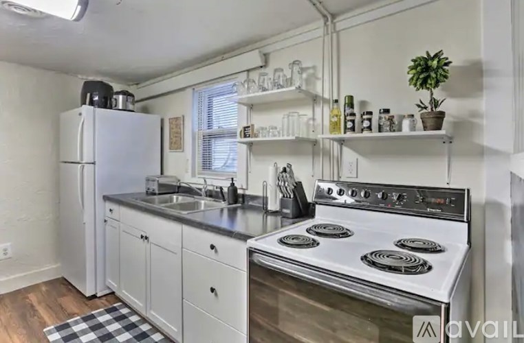 A kitchen with a white fridge, white cabinets, and a black and white checkered mat on the floor.