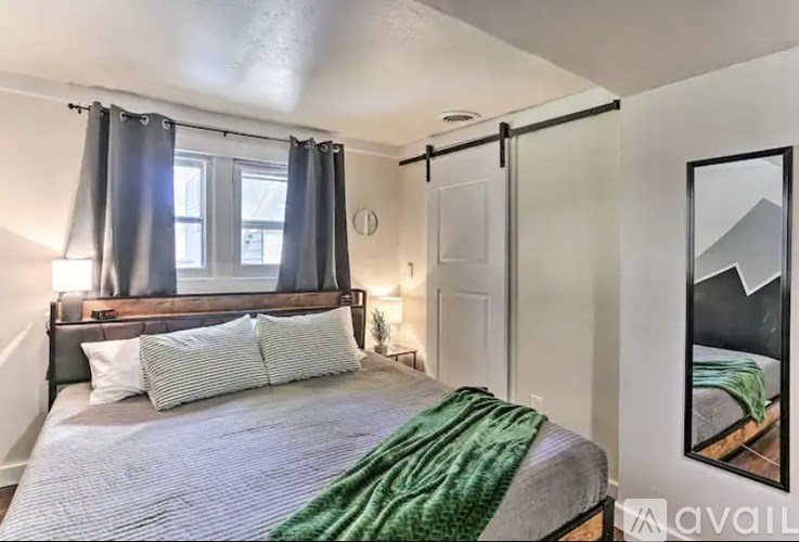 A bedroom with a bed, a mirror, and a window with curtains.