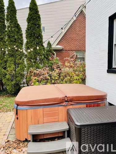 A hot tub sits in a backyard with a white house and trees in the background.