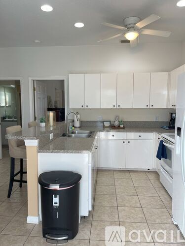 A kitchen with white cabinets and a black trash can.