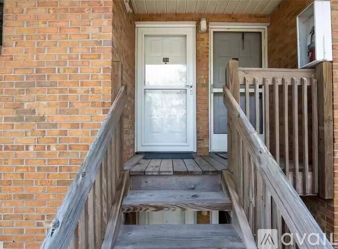 A wooden staircase leads to a white door on a brick building.
