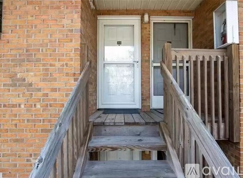 A wooden staircase leads to a white door on a brick building.