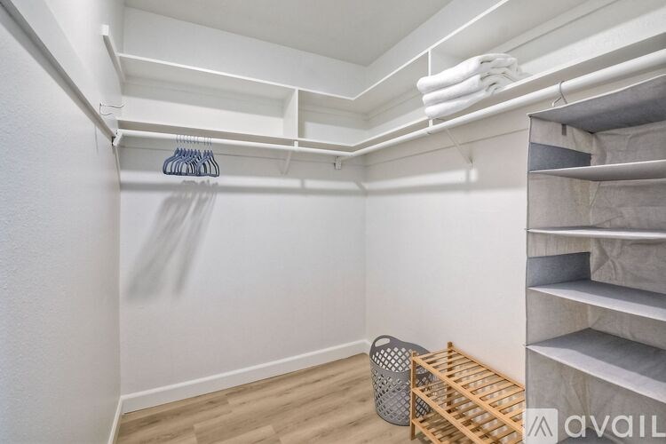 A room with a white wall and a wooden floor with a basket and a rack of clothes.