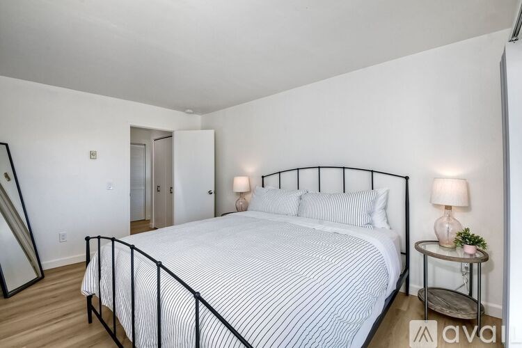 A bedroom with a large bed and a small table with a lamp on it.