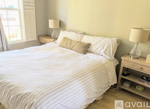 A bed with a white comforter and two pillows sits in a room with a nightstand beside it.