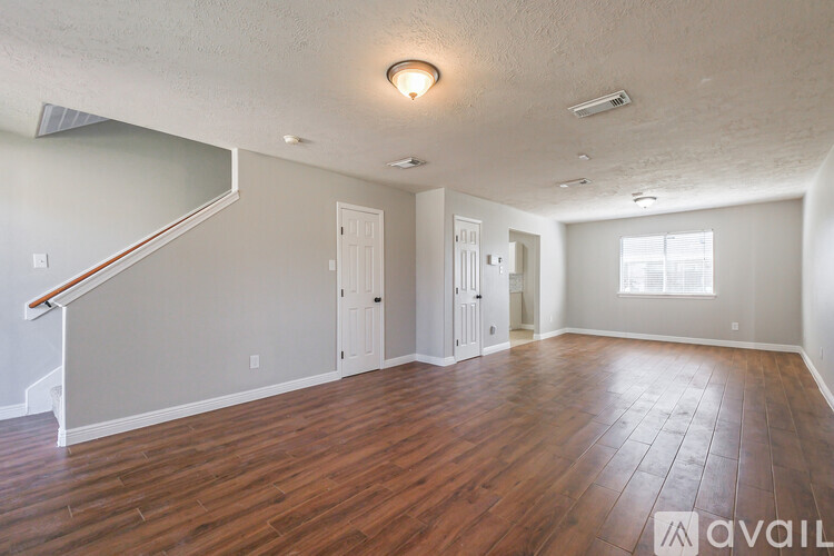 A spacious room with wood flooring and a staircase on the left side.