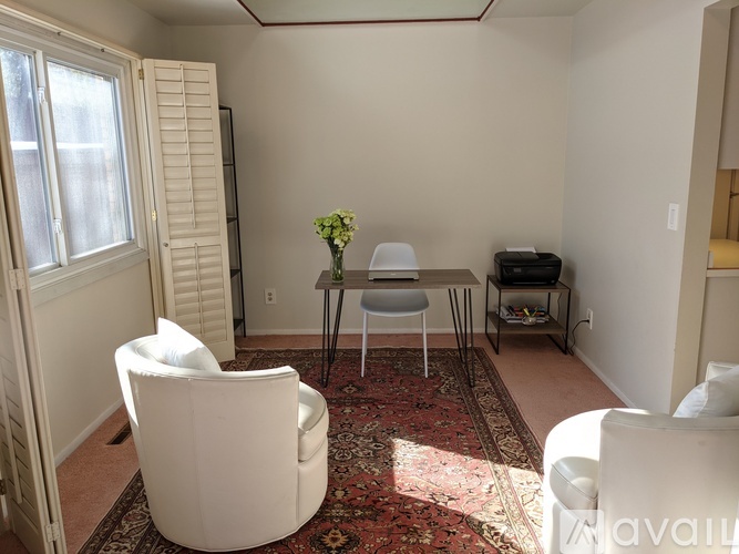 A living room with a white chair, a white sofa, and a small table with a vase of flowers on it.