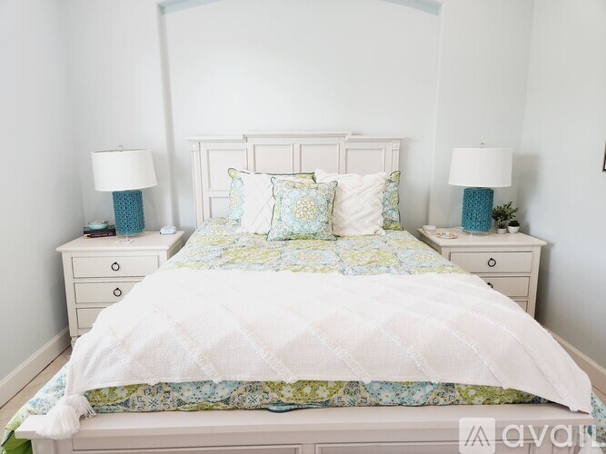 A white bed with a white headboard and a white comforter with a blue and green pattern on it.