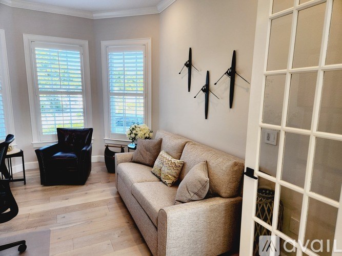 A living room with a beige couch, two chairs, and a wall decoration.