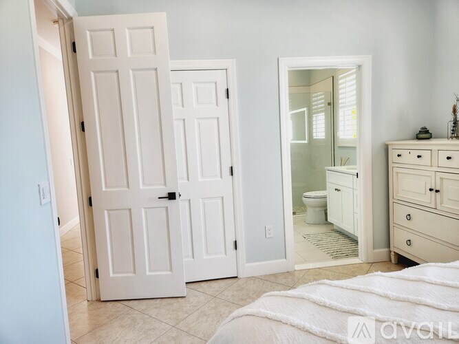 A white bedroom with a bed, dresser, and mirror.