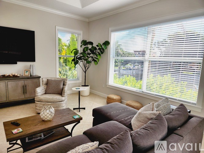 A living room with a brown couch, a wooden coffee table, and a large window with blinds.