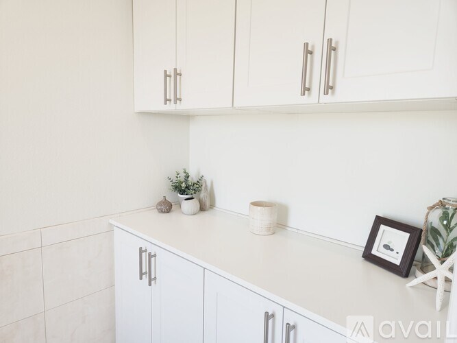 A kitchen with white cabinets and a white countertop with a plant and a picture frame on it.