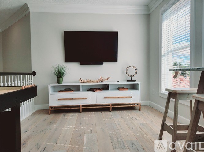 A living room with a wooden floor and a white wall with a flat screen TV mounted on it.