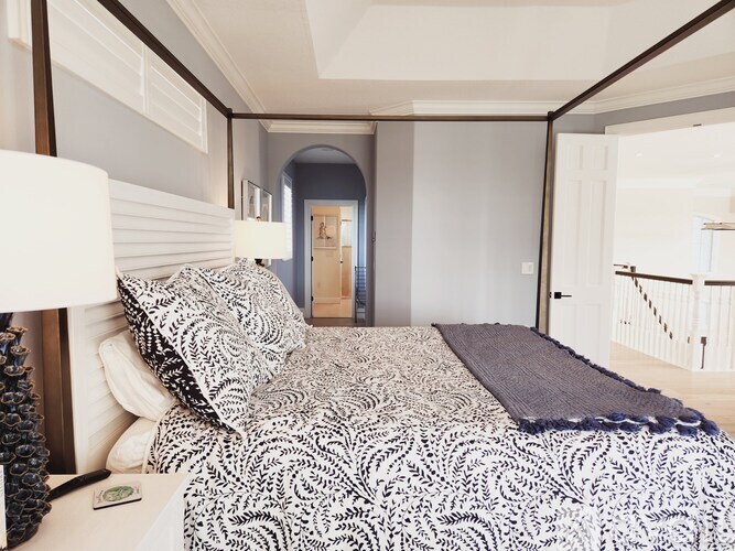 A bed with a black and white patterned comforter sits in a room with a wooden floor and white walls.