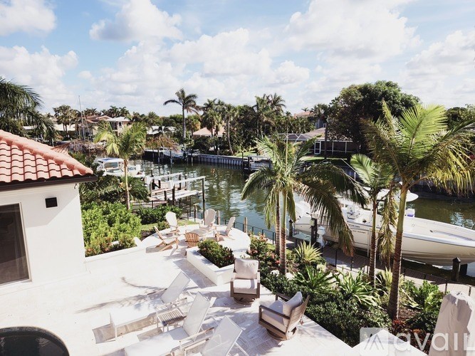 A patio with white furniture and palm trees overlooks a body of water.