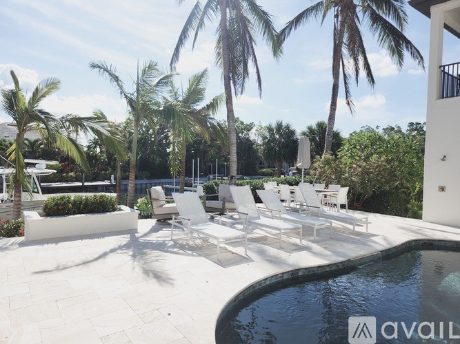 A pool area with white chairs and palm trees.