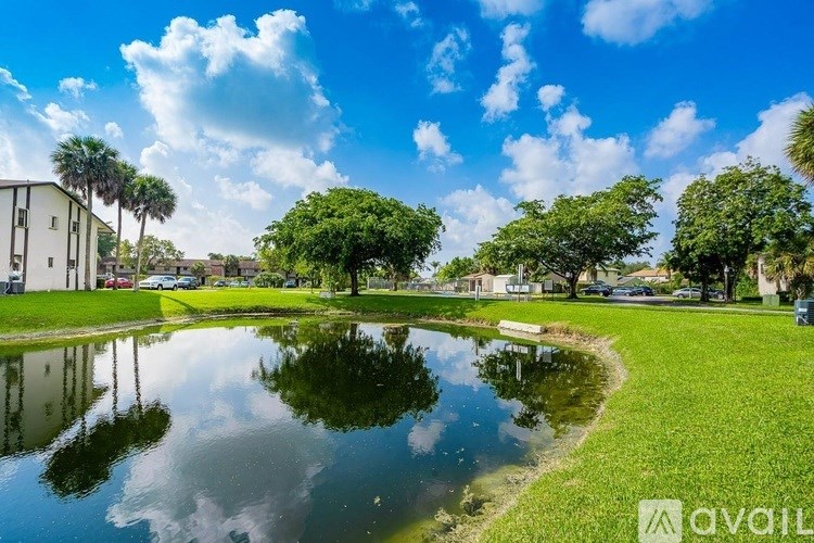 A serene park with a pond, trees, and a building in the background.