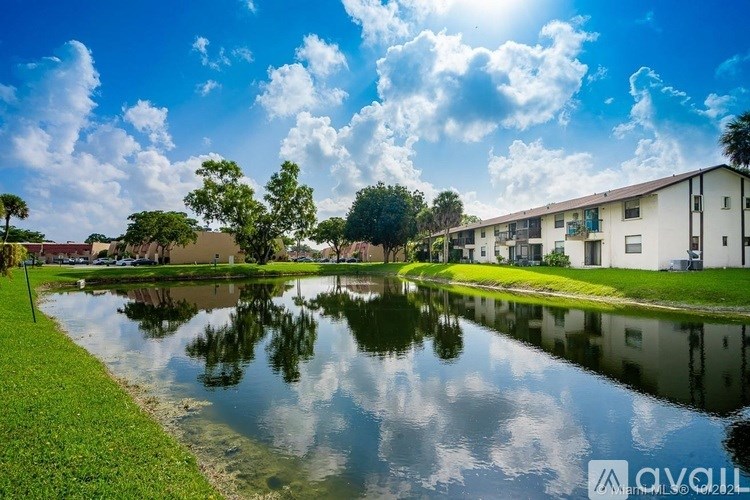 A serene lake in front of apartment buildings under a clear blue sky.