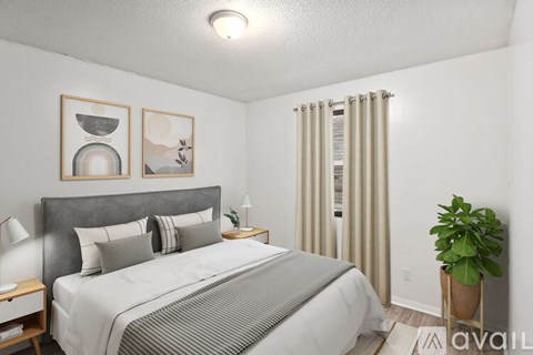 A bedroom with a large bed, a potted plant, and two framed pictures on the wall.