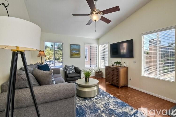 A living room with a grey couch, a round coffee table, a ceiling fan, and a flat screen TV.