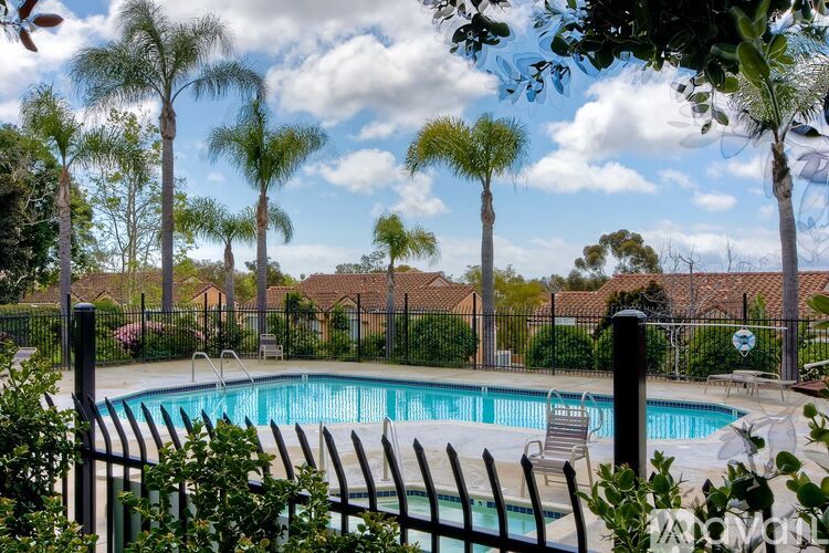 A pool surrounded by a black fence with trees in the background.