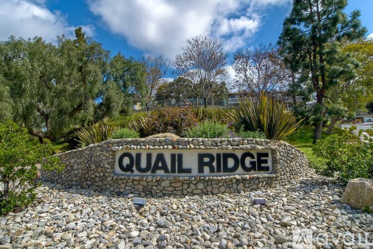A stone sign that says Quail Ridge in front of some trees.