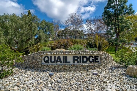 A stone sign that says Quail Ridge in front of some trees.