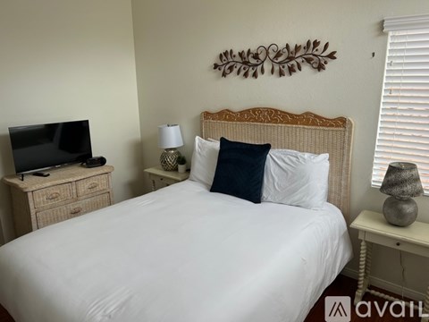 A bedroom with a white bed, a television on a cabinet, and a wall decoration.