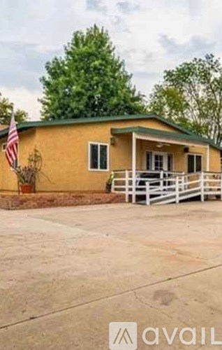 A yellow house with a green roof and a white fence.