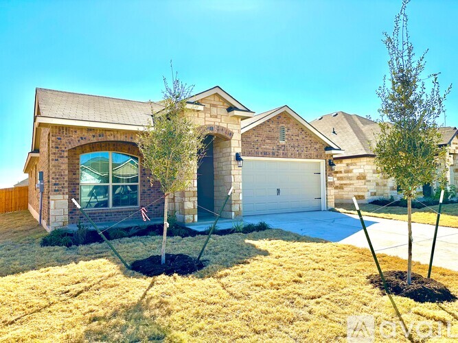 A house with a garage and a driveway is surrounded by grass and young trees.