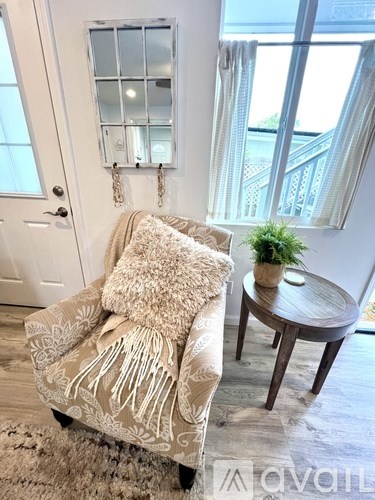 A beige couch with a pillow and throw on it sits in a room with a small table and a window.