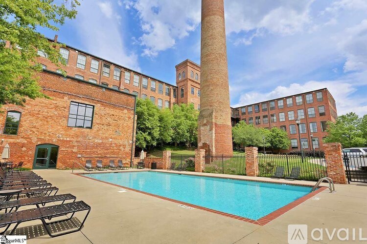 A large brick building with a tall brick chimney and a pool in front.