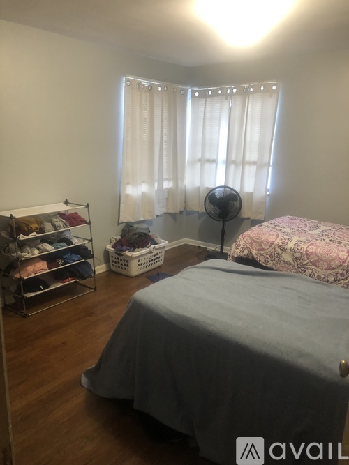A bedroom with a bed, a fan, and a shoe rack.