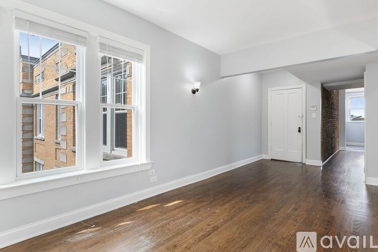 A room with wooden floors and white walls, with a window showing a building outside.