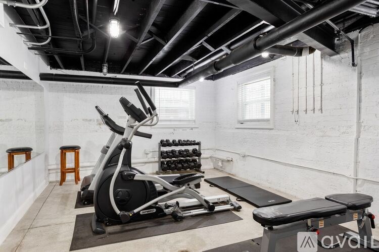 A gym with a rowing machine, dumbbells, and a bench.