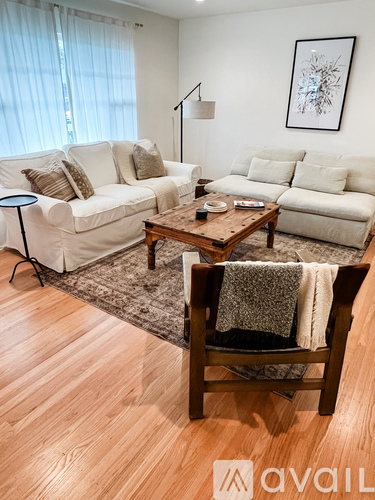 A living room with a white couch, a wooden coffee table, and a chair with a blanket on it.