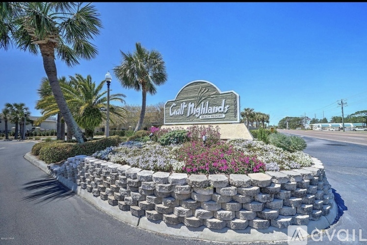A sign that says "Gulf Highlands" is surrounded by a flower bed and palm trees.