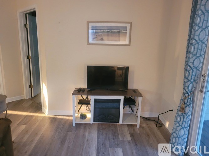 A black television is on a white stand in a room with light wood flooring.