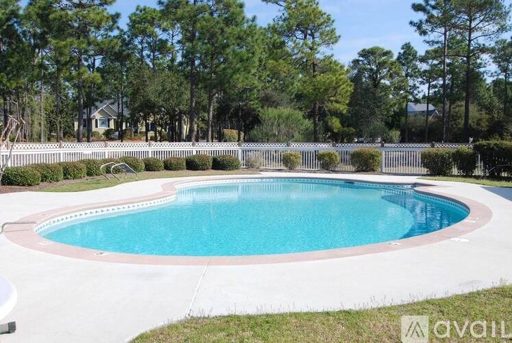 A round above ground pool surrounded by a white fence and green trees.