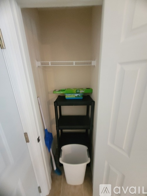 A small white door with a black shelf and a white bucket in front of it.