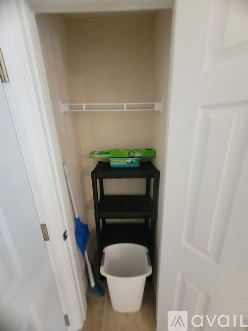 A small white door with a black shelf and a white bucket in front of it.