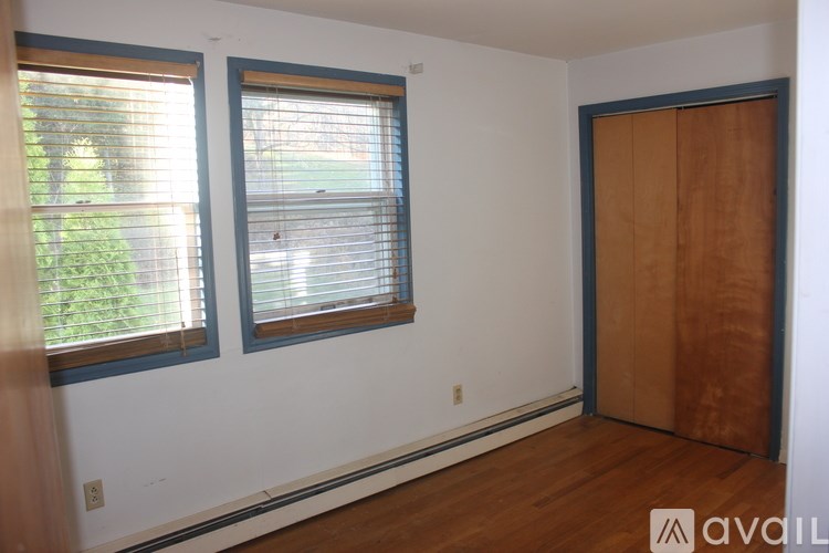 A room with a wooden floor, a window with blinds, and a wooden door.