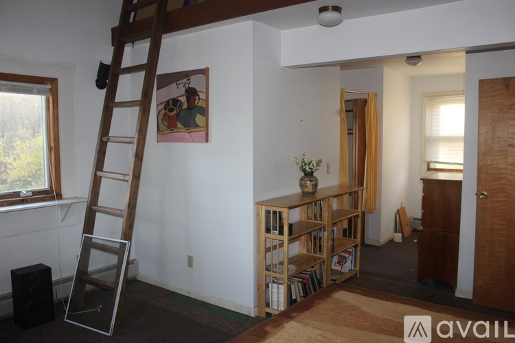 A room with a ladder, bookshelf, and a painting on the wall.