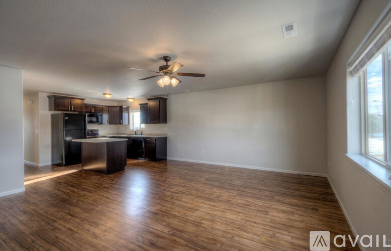 A spacious living room with a kitchen in the background and a ceiling fan above.