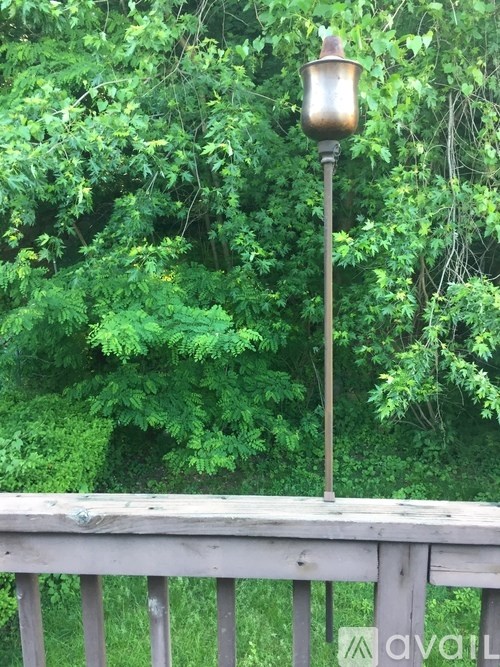 A lamp post on a wooden deck with green trees in the background.