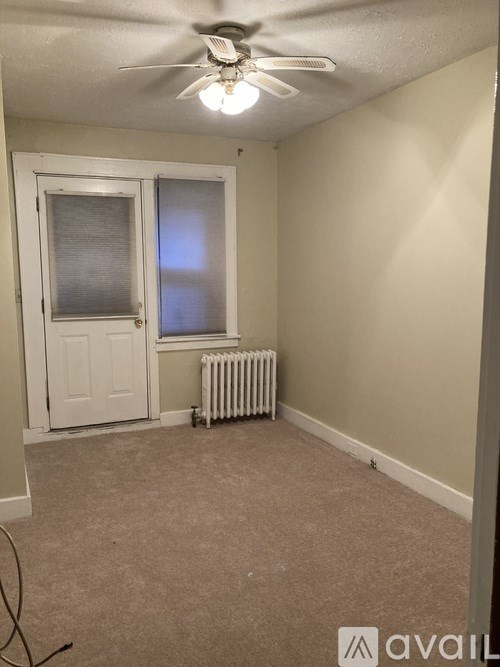 A room with a fan, a window with blinds, and a radiator on the floor.