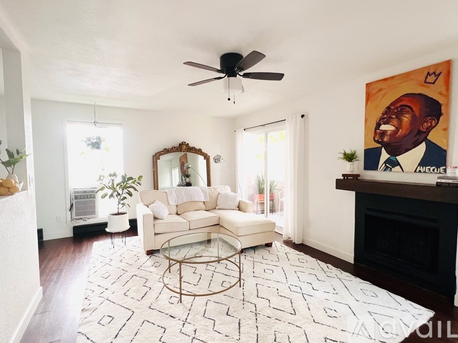 A living room with a white couch and a painting of a laughing man on the wall.