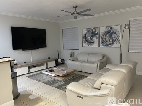 A living room with a white couch, a coffee table, and a flat screen TV mounted on the wall.