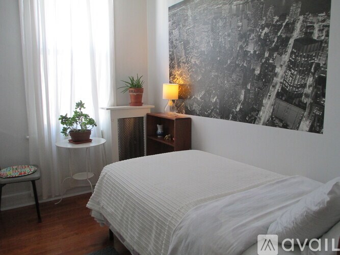 A bedroom with a bed, a chair, a potted plant, and a wall with a black and white photo.