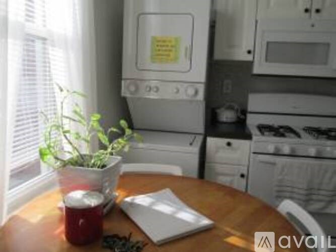 A small table with a laptop, a red mug, a potted plant and a note on the fridge.
